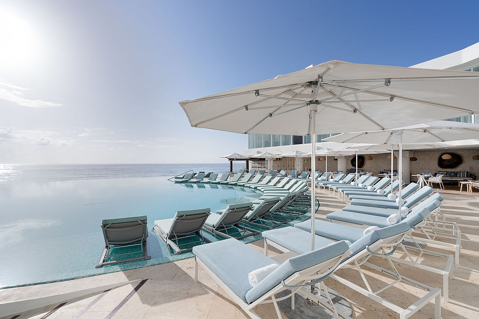 Sunlit poolside with empty blue loungers and umbrellas overlooking the ocean, creating a tranquil and relaxing atmosphere.