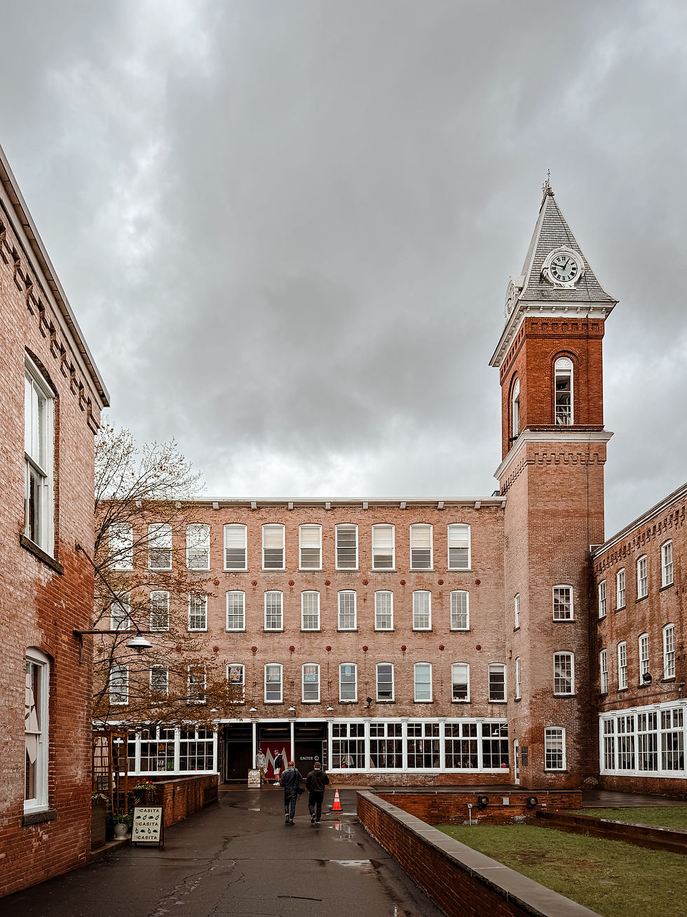 Two people walk toward a brick building with a clock tower on a cloudy day. A sign reads "MOCA B52 CAFE & SANTA CAFETA."