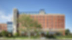 Red brick hotel with "The Asbury" sign, tree in foreground, clear blue sky, and modern glass windows. Calm urban setting.