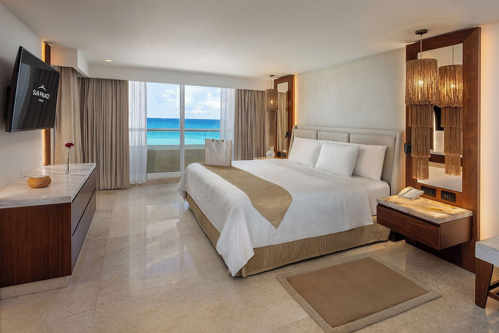 Luxurious hotel room with a king bed, beige decor, ocean view through large windows, and a "Sun Palace" logo on the TV. Calm and inviting.