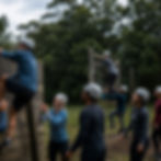 People in helmets climbing an outdoor obstacle course.