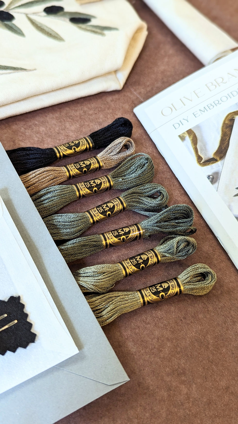 A flat lay photograph showing sustainable embroidery kit materials: DMC embroidery thread, organic cotton, and instruction booklet.