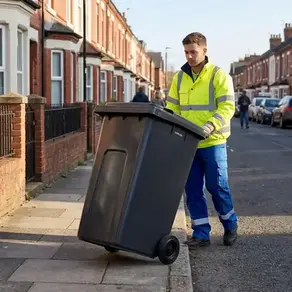 A man pushing a 240L black wheelie bin