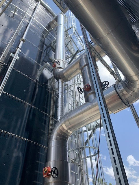 Industrial insulated pipes and tanks shot from below against a blue sky