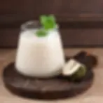 Creamy white drink in a glass with mint garnish, on wooden board. Brown background, piece of soursop beside the glass. Cozy setting.