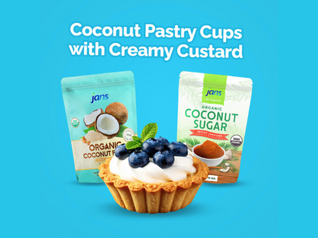 Coconut pastry cup with blueberries and mint on creamy custard, set against a blue background with packages of coconut flour and sugar.