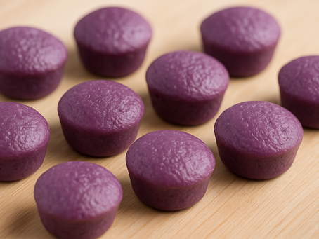 Ten purple ube muffins on a light wooden surface. The muffins have a smooth texture and are evenly spread, creating a cozy, inviting mood.