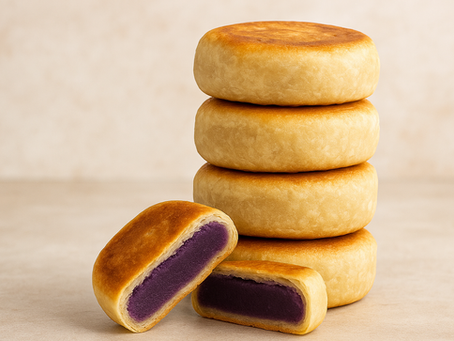 Stack of round pastries with a golden crust and purple filling, set against a beige background. One pastry is cut to reveal the filling.