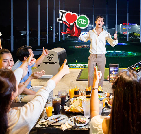 Man posing in front of colleagues at an offsite event with a custom 'I heart QB' prop.