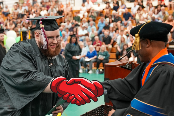 Graduate poses with handshake prop with president as he receives his diploma