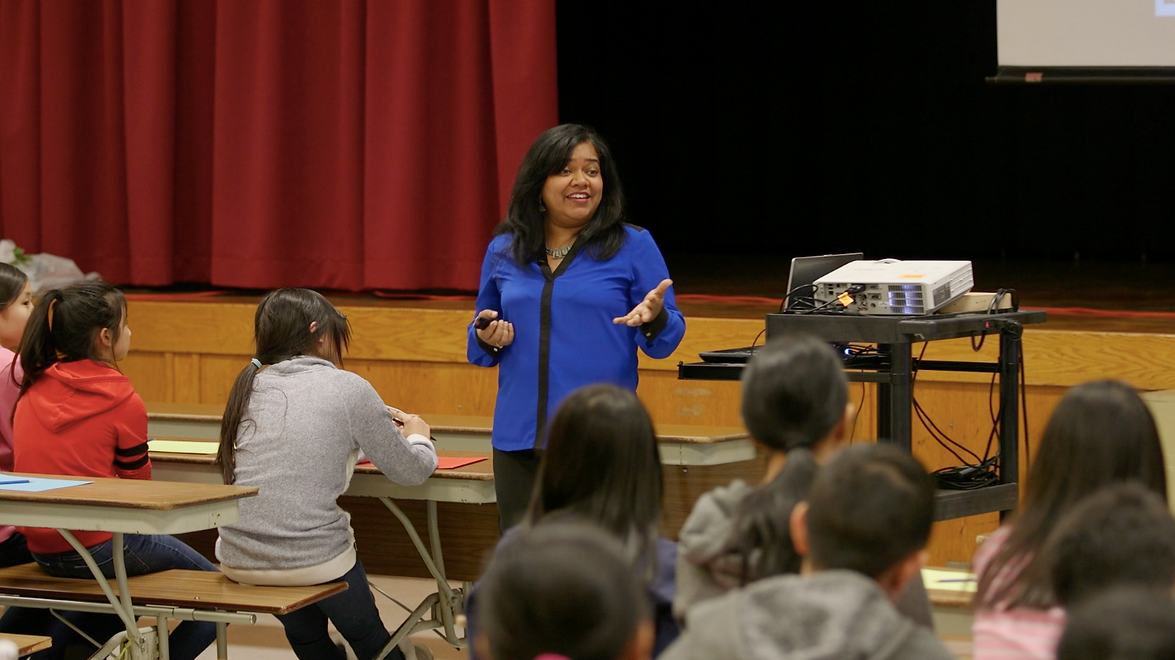 An image of professional speaker, Keka DasGupta, wearing a royal blue-coloured blouse, smiling and speaking to students during a school workshop on Gratitude