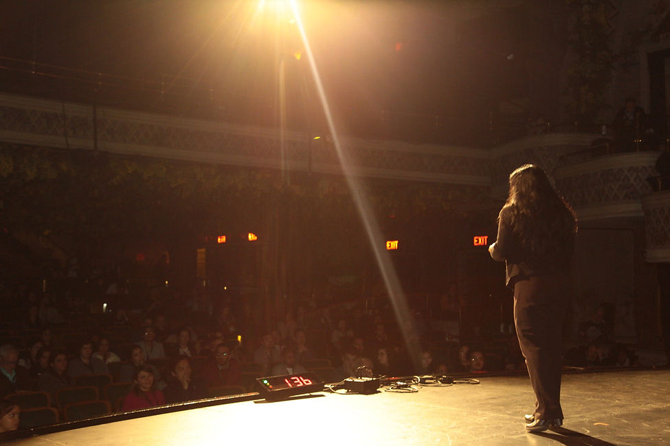 An image of Keka DasGupta speaking on stage at the Socialight Conference, taken from behind the stage at Toronto's famous Winter Garden Theatre