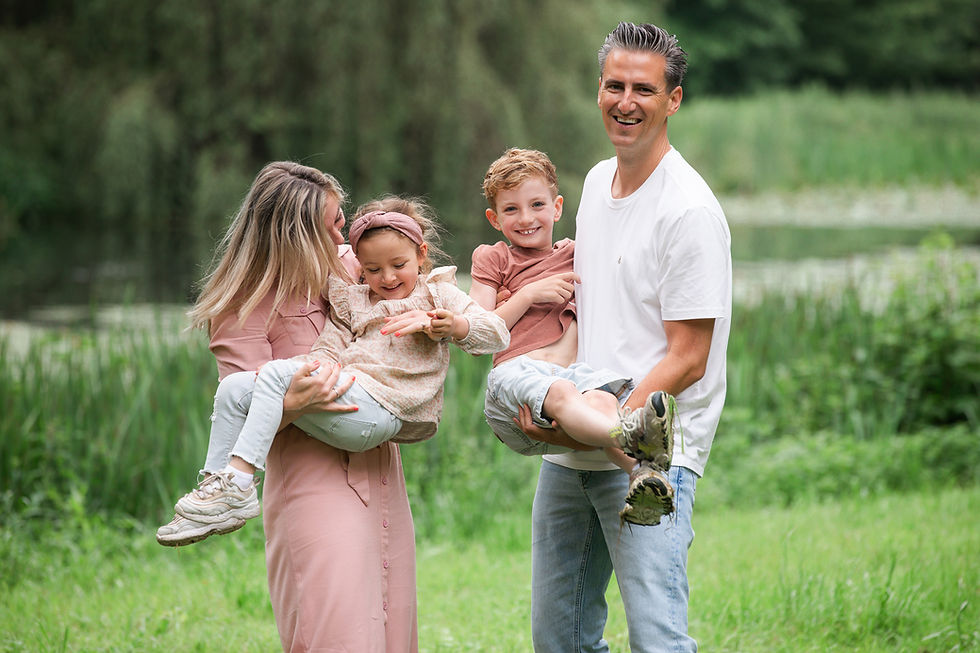 Lachend gezin met twee kinderen op de arm in een groen park bij water; ontspannen en vrolijke sfeer