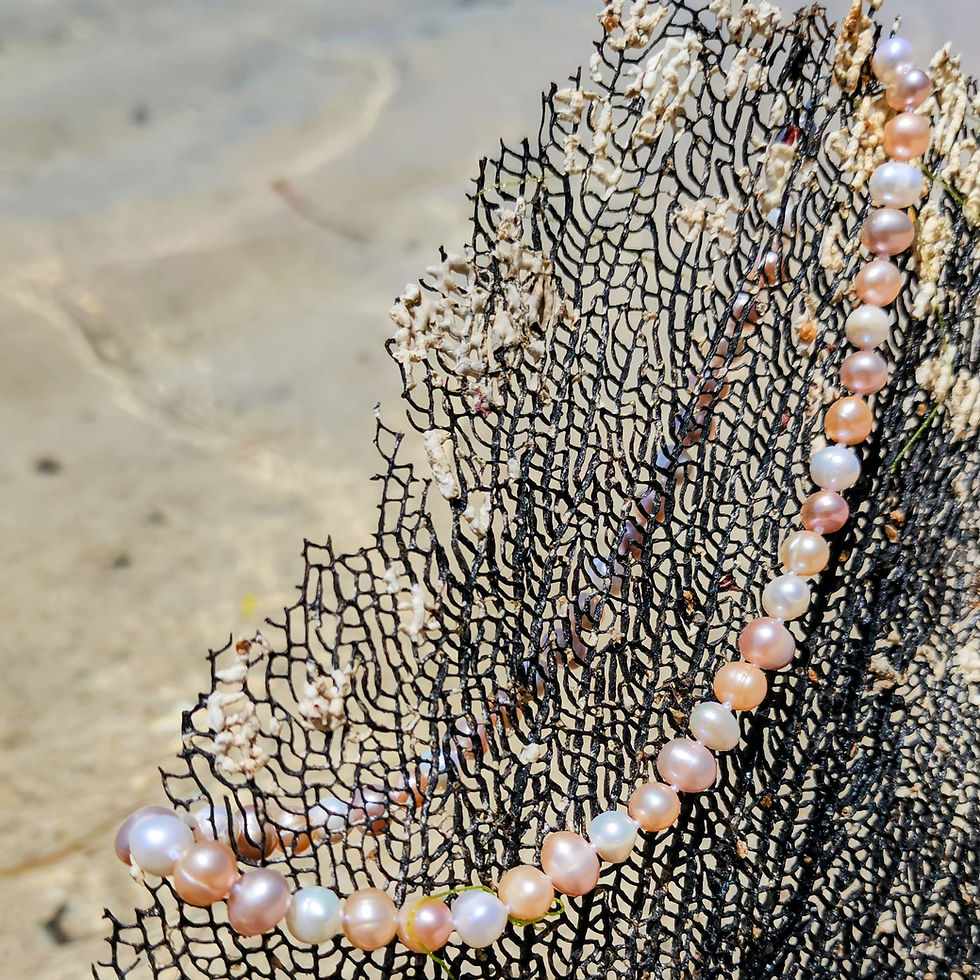 White and peach pearl necklace on a dark coral, background of water and sand.