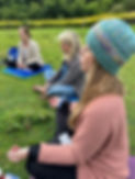 Three women sitting on the grass meditating.