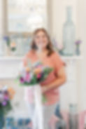 Smiling woman holding colorful bouquet, standing in front of mantelpiece.