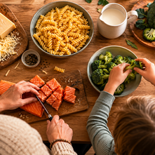 Elternteil und Kind bereiten gemeinsam Lachs, Brokkoli und Nudeln auf einem Holztisch zu – Ernährung im Familienalltag bei ADHS.