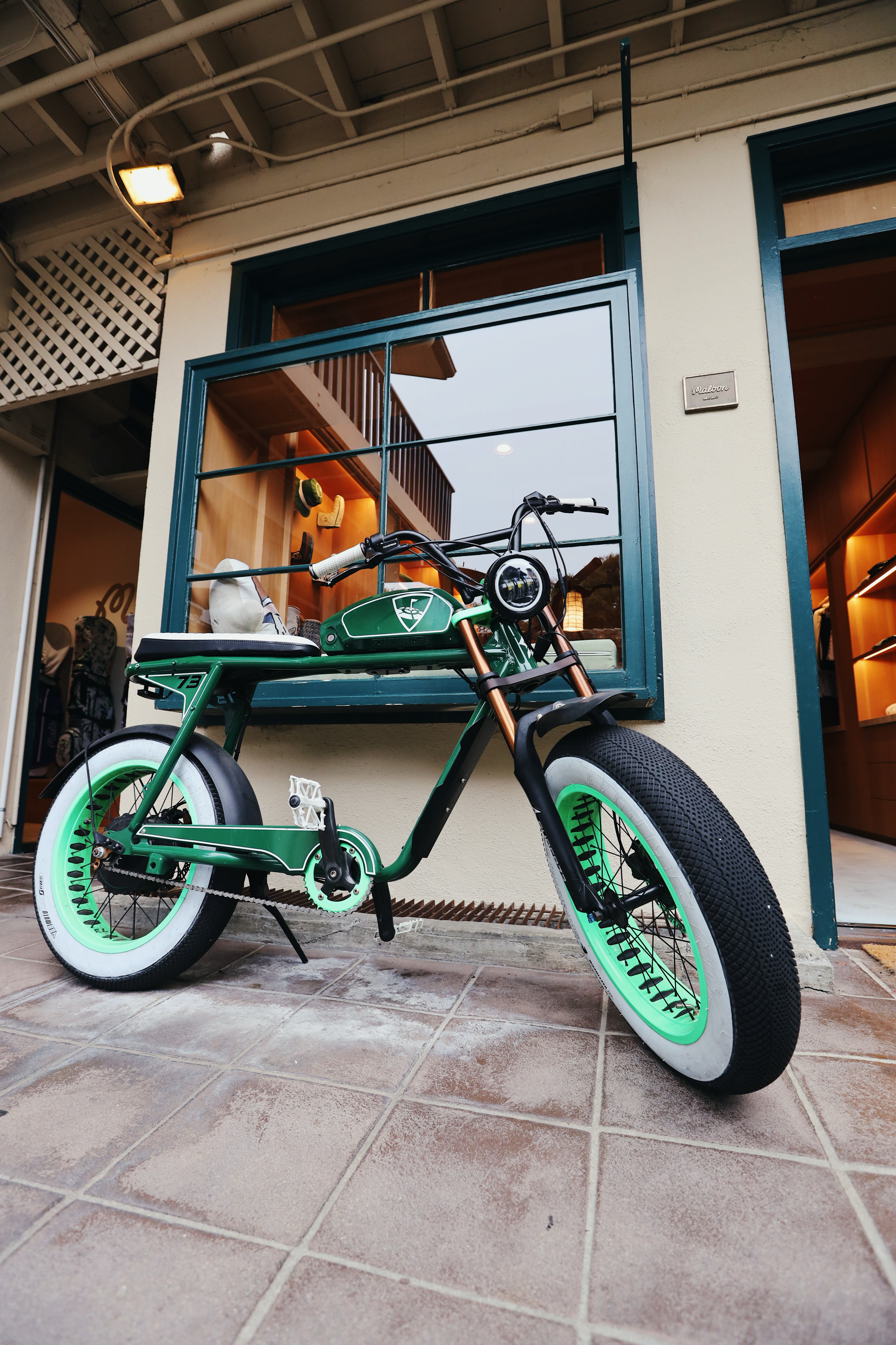 A custom green Malbon Golf Fatcat bike with whitewall tires parked outside the Malbon Golf store in Carmel, California, showcasing golf lifestyle, streetwear, and skate-inspired design.