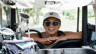 A women smiling from inside a golf cart.