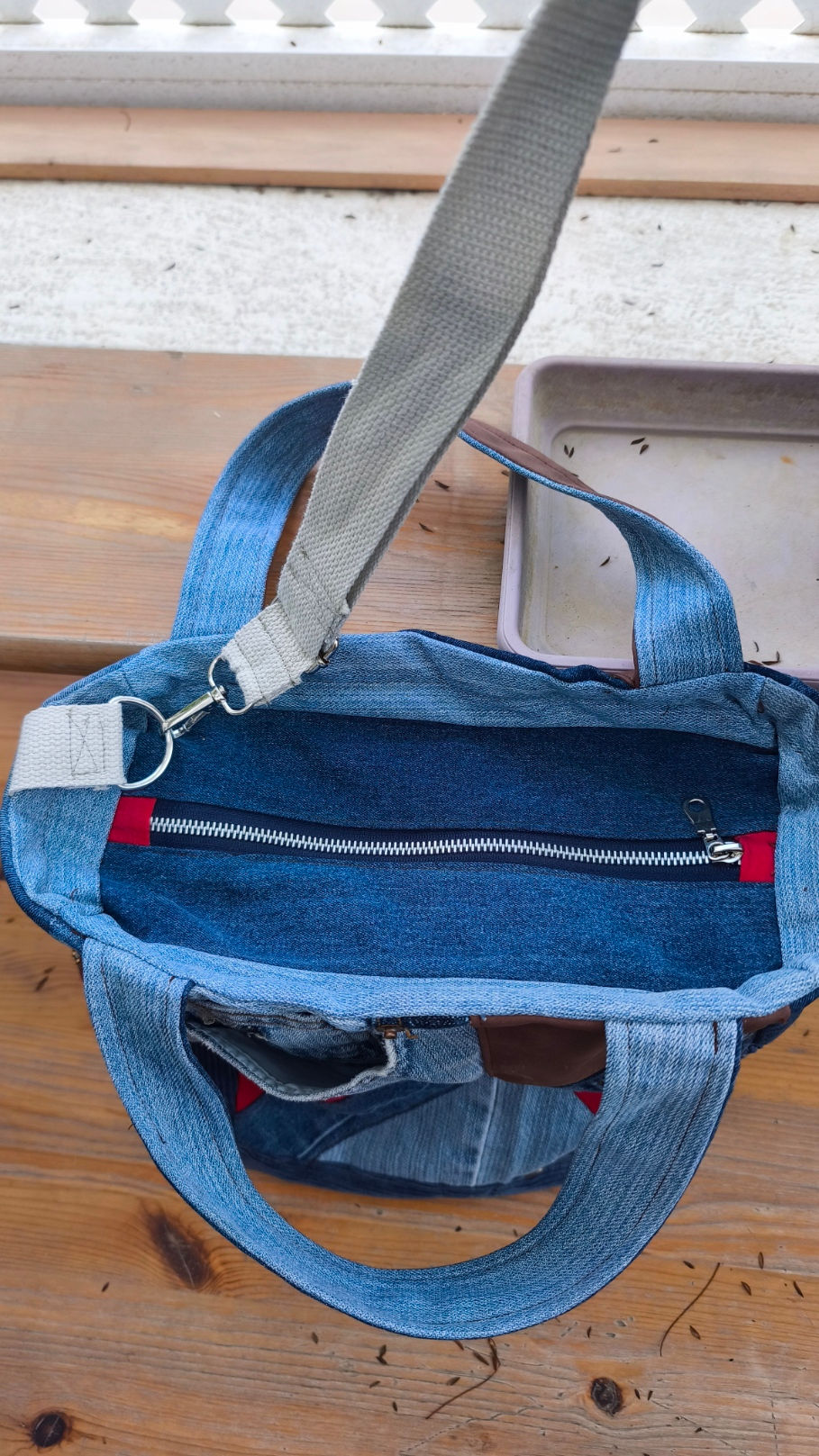 Tote bag, made from recycled denim in various shades of blue and a touch of red. Featuring a V-shaped faux leather patch and a denim and caramel-colored leather handle.