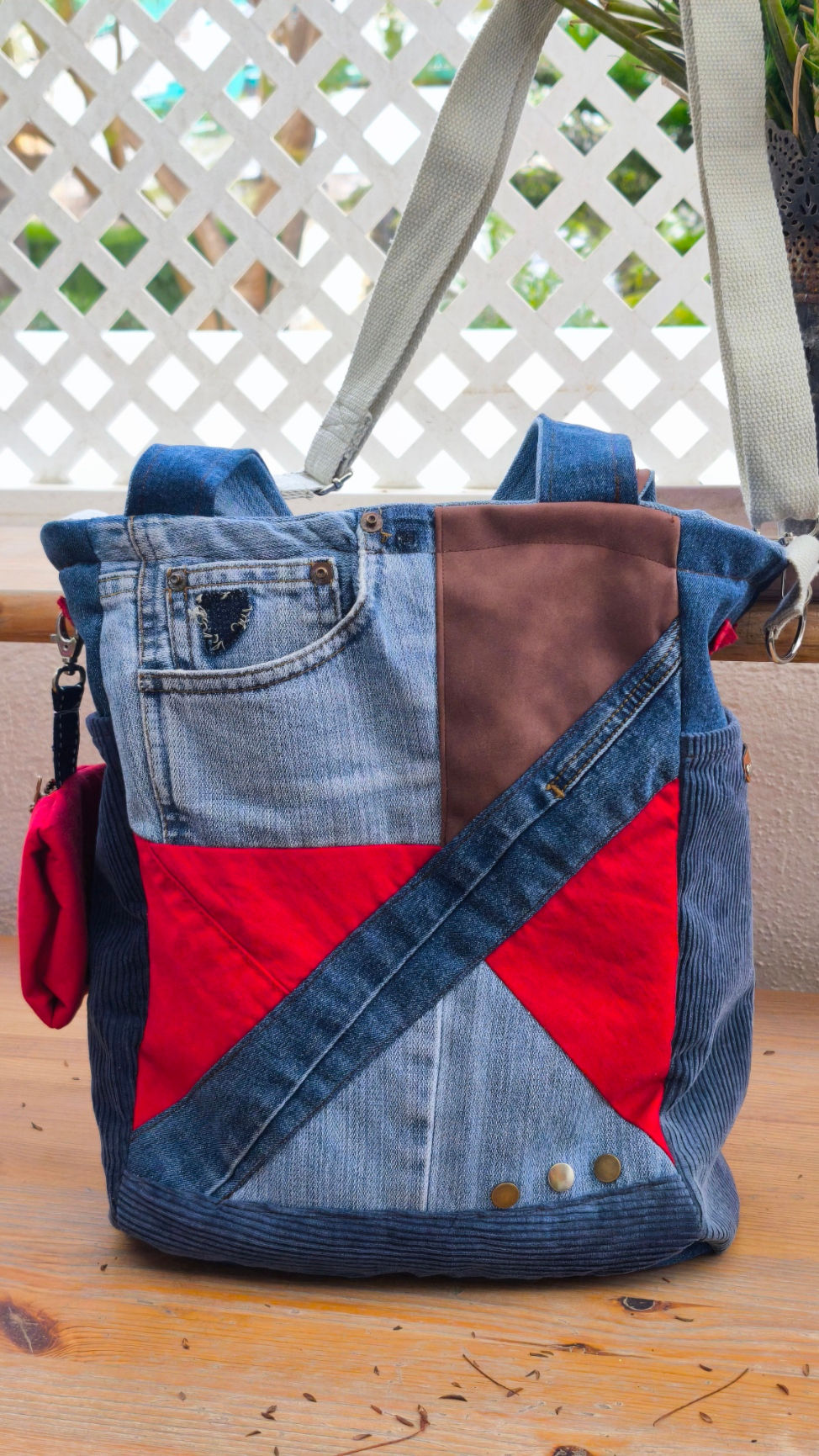 Tote bag, made from recycled denim in various shades of blue and a touch of red. Featuring a V-shaped faux leather patch and a caramel-colored denim and leather handle.