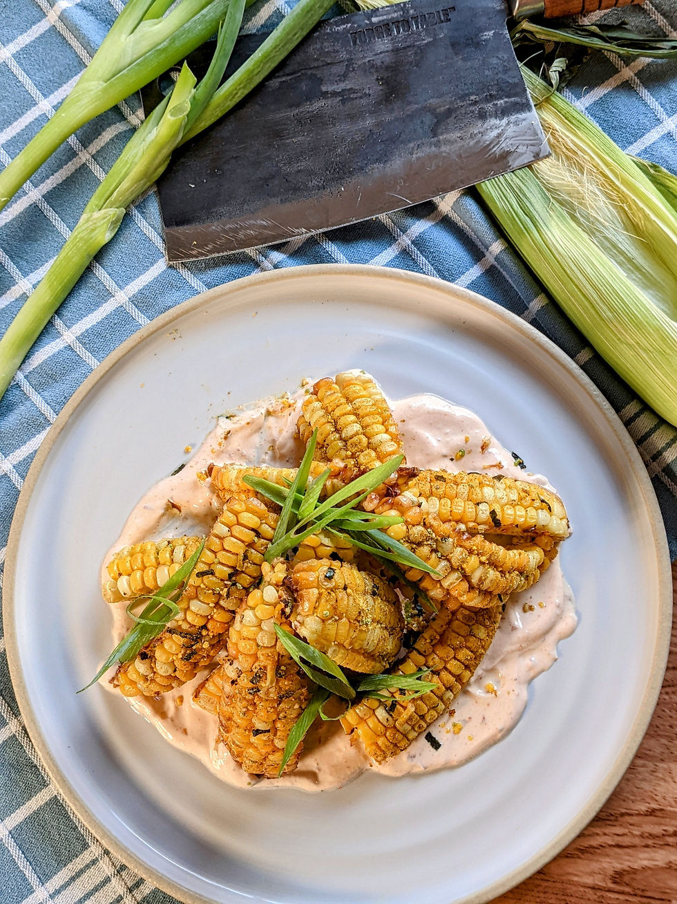 Plate of grilled corn on creamy sauce with green garnish; cleaver marked TOGETHER and corn husks on a blue checkered cloth.