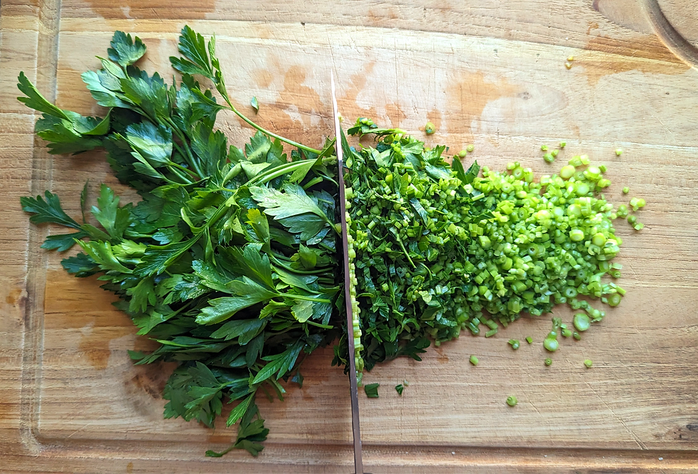 Fresh parsley being chopped on a wooden cutting board, showing vibrant green leaves and finely diced herbs.