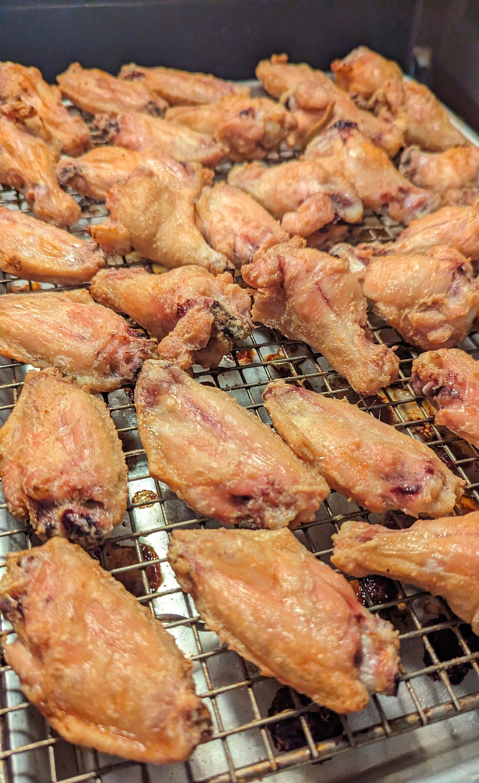 Golden-brown chicken wings on a wire rack, baked and crispy, in a kitchen setting. The wings are evenly spaced with a focus on texture.