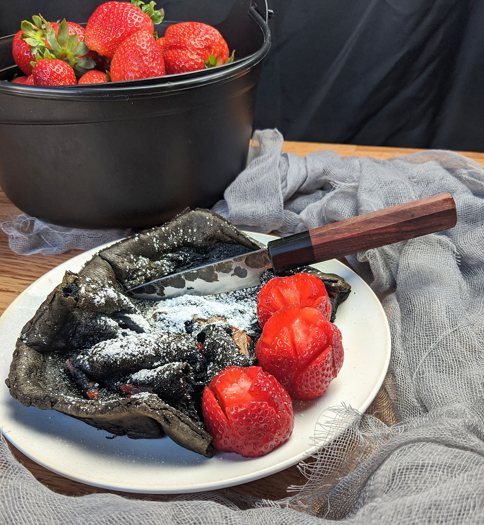 Black crepe on a white plate with strawberries and a knife, beside a bucket of fresh strawberries on a wooden table.