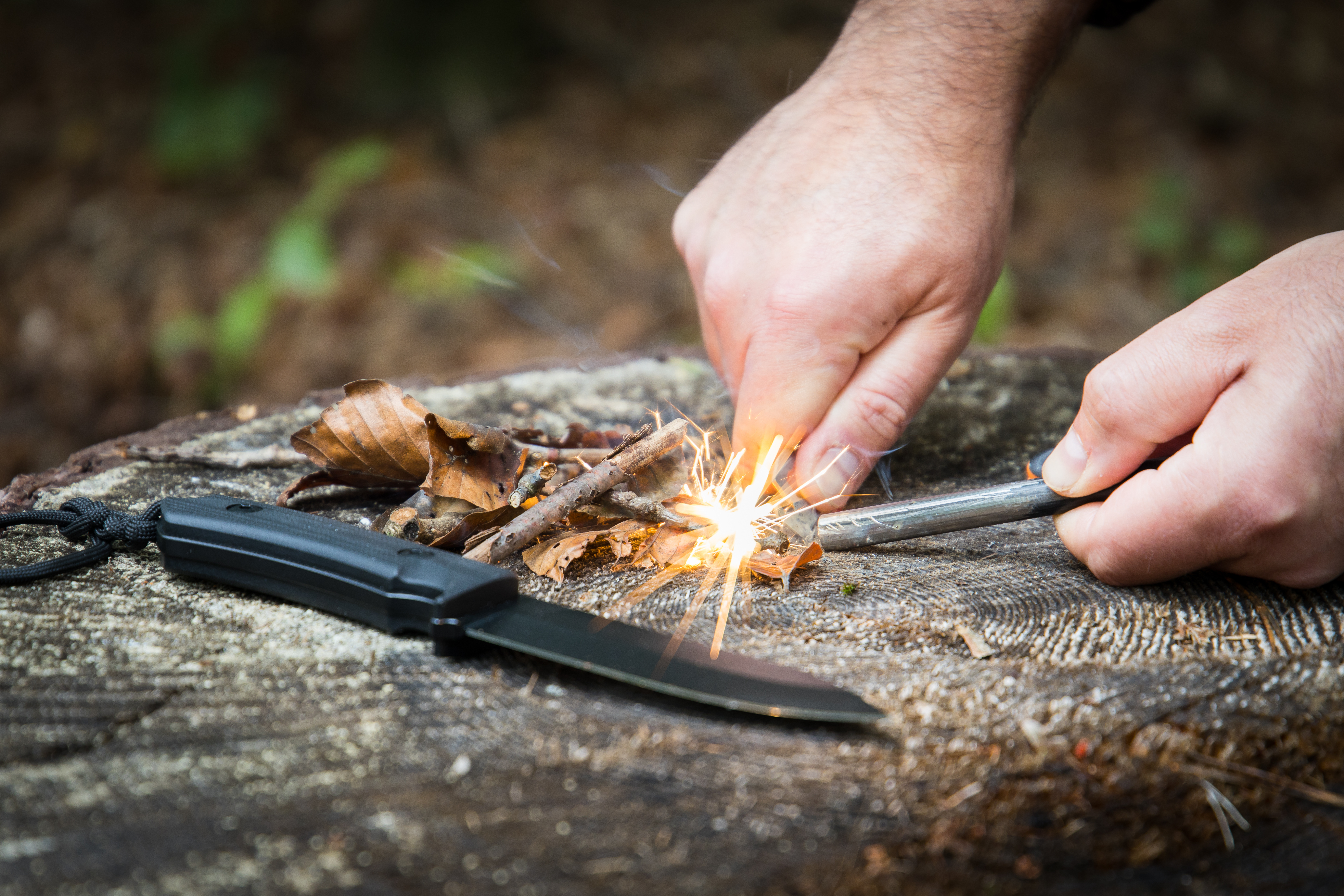 Men hand starts fire with magnesium fire steel in the woods