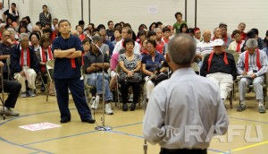 Dr. Takeshi Matsumoto listens as Shawn Miyake (foreground), CEO and president of Keiro Senior Healthcare, speaks during a public forum on Thursday at Nishi Hongwanji Buddhist Temple in Little Tokyo. Below: An audience member yells out a comment during the presentation. Many wore red strips of cloth to indicate their opposition to the sale of Keiro’s facilities.