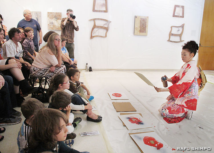 スプレーを使い、色紙に椿の葉を描く平野さん(右)のパフォーマンスを凝視する参加者