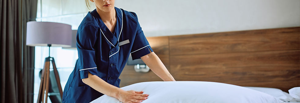 Young female housekeeper making bed in h