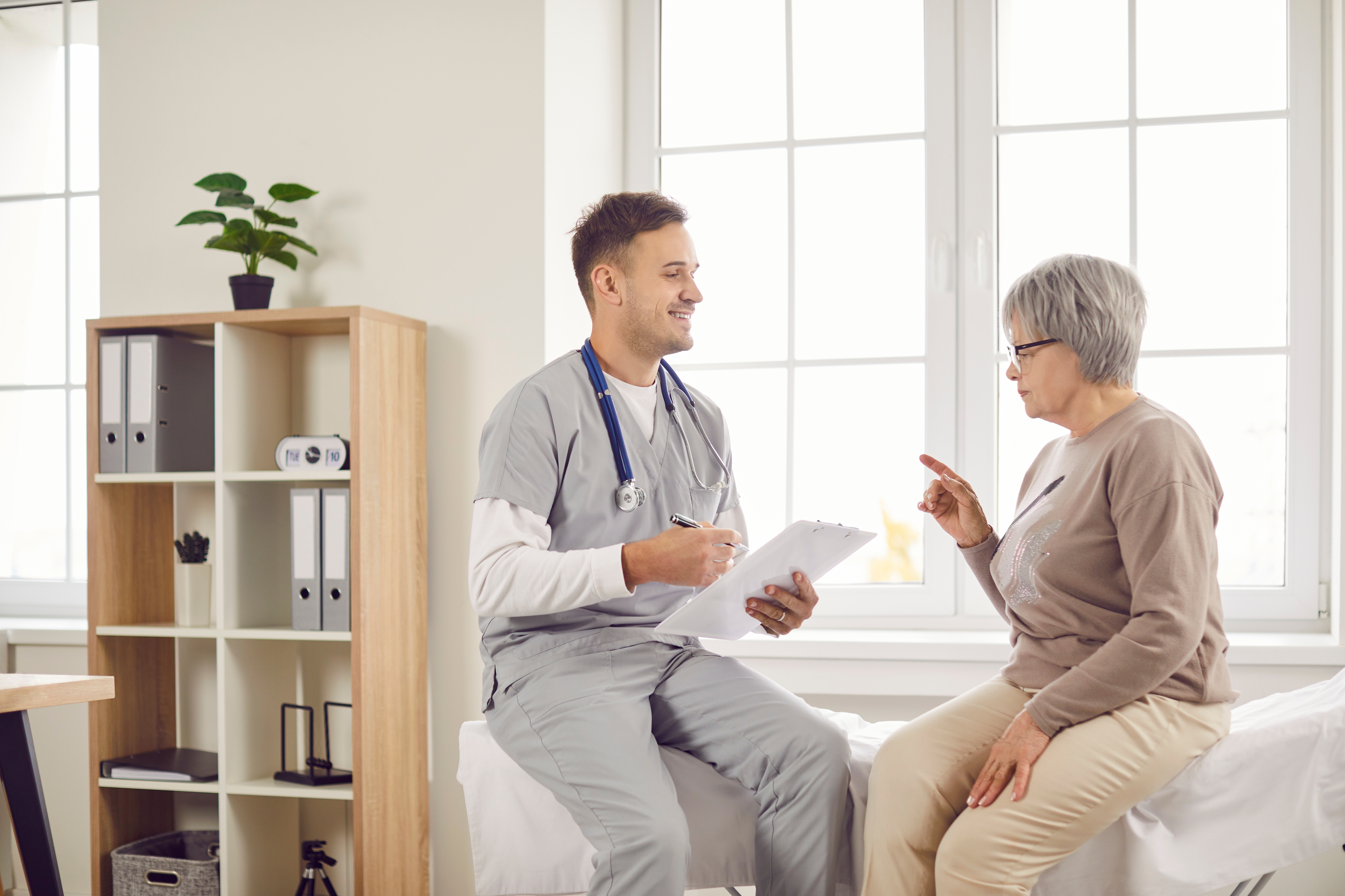 Young happy doctor, male nurse and old woman talking, explaining, taking social healthcare