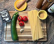 Alle Zutaten für ie Zucchini-Tomaten-Pasta sind auf einem Holzbrett ästethisch angerichtet.