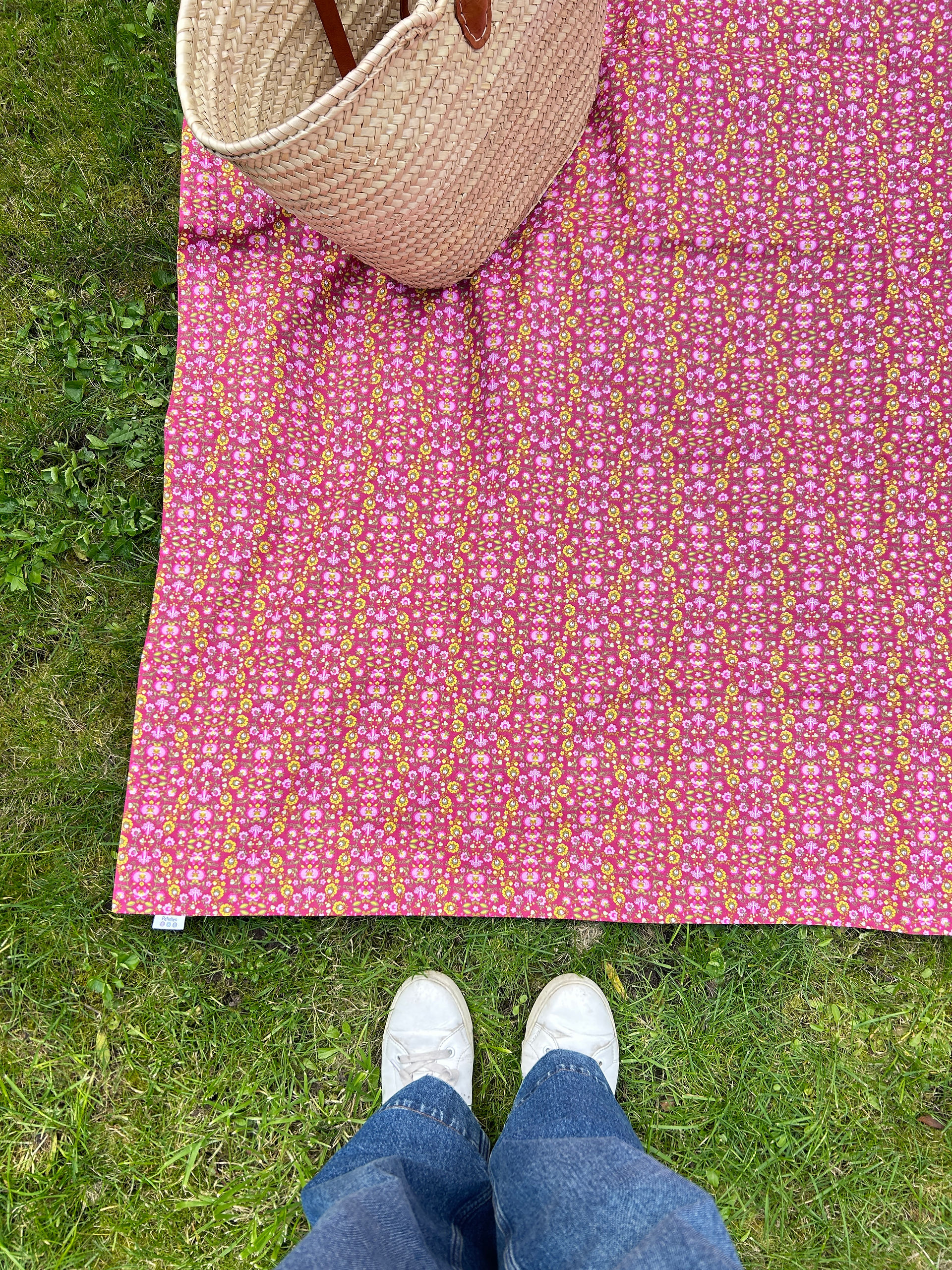 Pink floral waterproof picnic blanket laid flat on grass — cotton top detail, Petiotes London