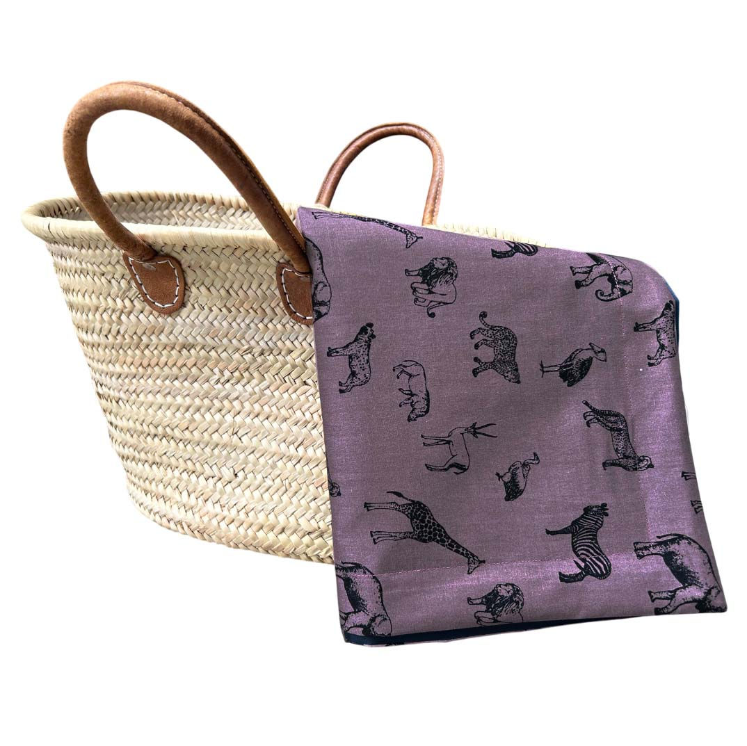 Overhead view of the Rosewood Safari picnic blanket folded neatly in a basket, showcasing its texture, colour, and stitched b