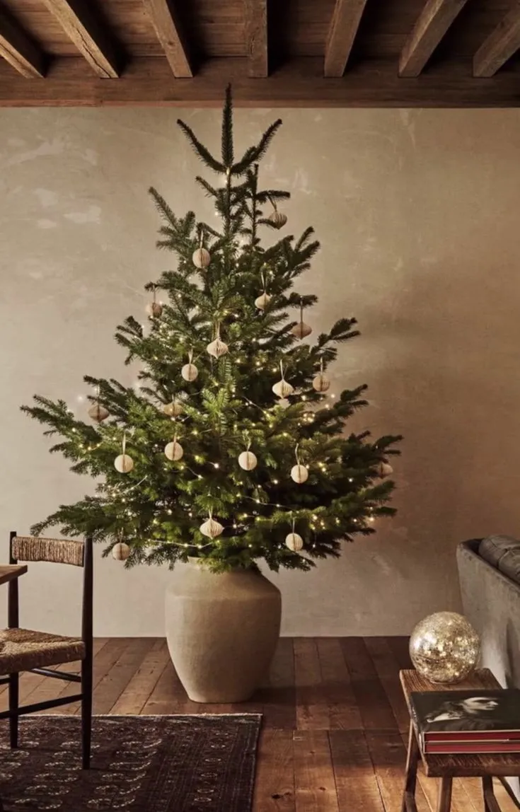 Minimal Christmas tree in ceramic pot with warm fairy lights and few ornaments — elegant, intentional décor.