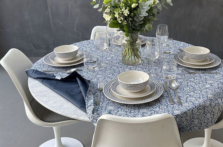 Waterproof outdoor blanket styled as a tablecloth with tableware and green flowers in a modern dining room.