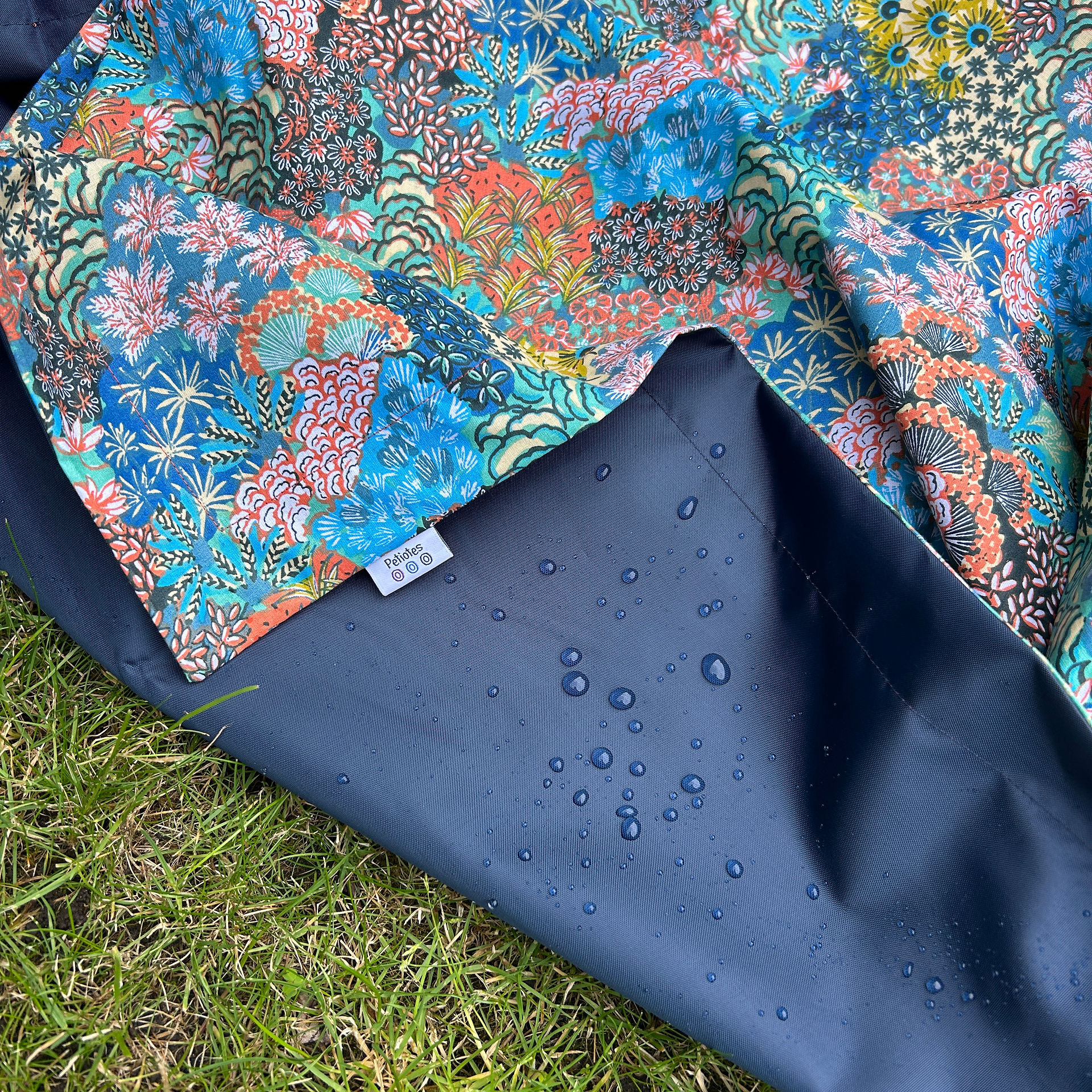 Close-up of PU waterproof backing with water droplets on damp grass — floral waterproof picnic blanket by Petiotes London