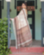 Back view of a woman in a designer print saree featuring a wide, beautiful brown and rust ethnic border and tassels.