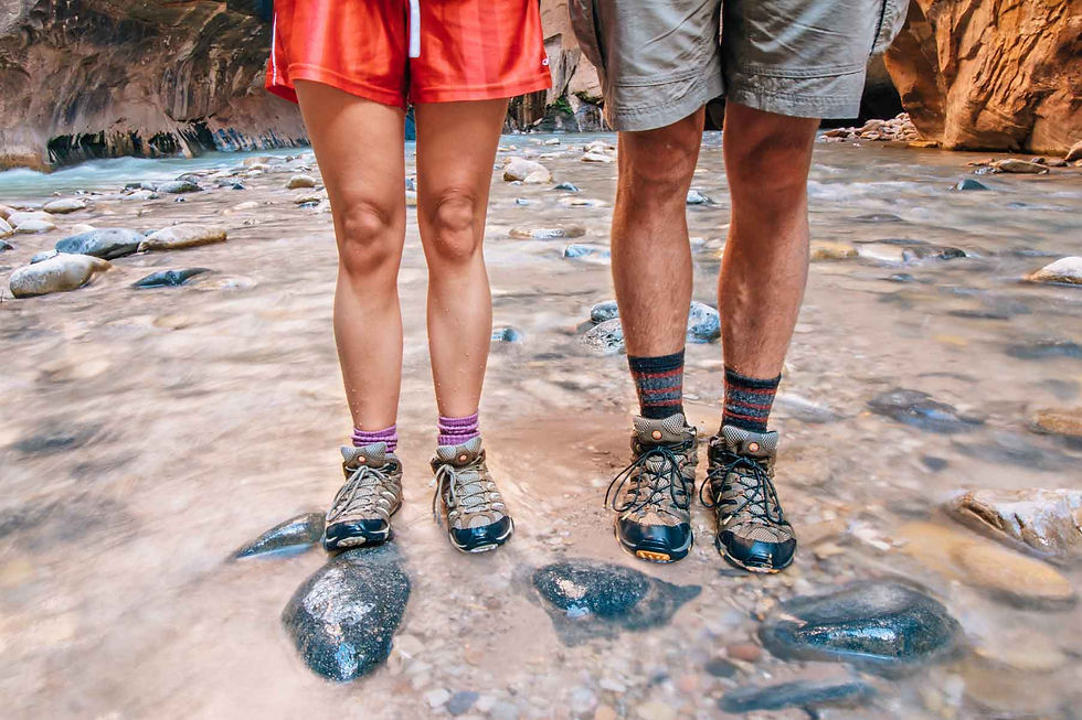 A picture of male and female hiking boots in the shallow edge of a creek.