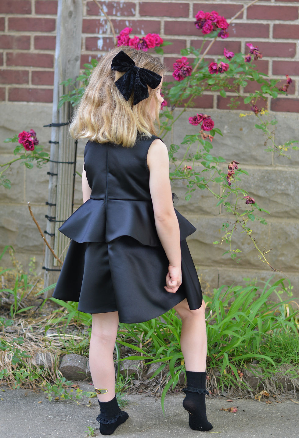 Thumbnail: Model wearing an Olivia Inspirations Black Dress with a peplum side view. 
