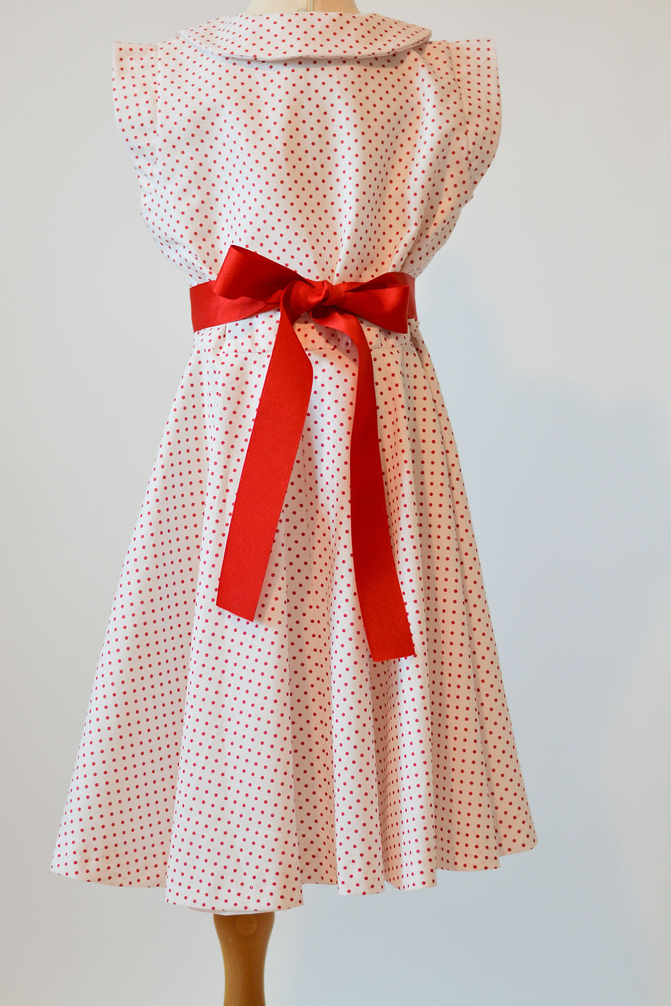 Thumbnail: An Olivia Inspirations white and red polka dot dress with red buttons, a red belt, back view.