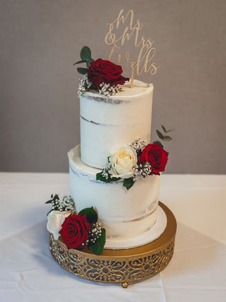 Large two tier semi-naked wedding cake with red and ivory roses and gypsophila, on a gold stand at Alexandra House. Flowers by Ivory Rose Florist.