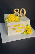 Elegant 80th birthday cake with ivory buttercream, yellow sugar flowers, gold accents and personalised message Happy Birthday Jan.