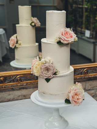 Small three tier semi-naked wedding cake with blush and ivory roses by Kopend Creations, displayed at Tortworth Court on a white cake stand.