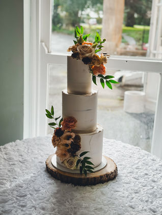 Small three tier buttercream wedding cake with warm-toned flowers and greenery by Fabulous Functions, displayed on a rustic log slice at Chiseldon House Hotel.