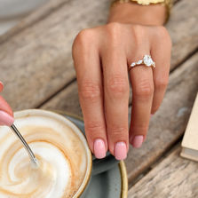 Bryony oval lab-grown diamond engagement ring worn on the hand beside a cup of coffee.