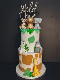 Two-tier jungle-themed fondant cake with handmade lion, elephant, monkey, giraffe, zebra and hippo toppers, and giraffe print and leaf decorations.